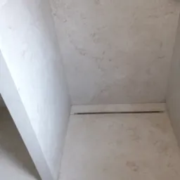 Wykończona kabina prysznicowa z odpływem liniowym i płytkami imitującymi kamień w odcieniach beżu i szarości.