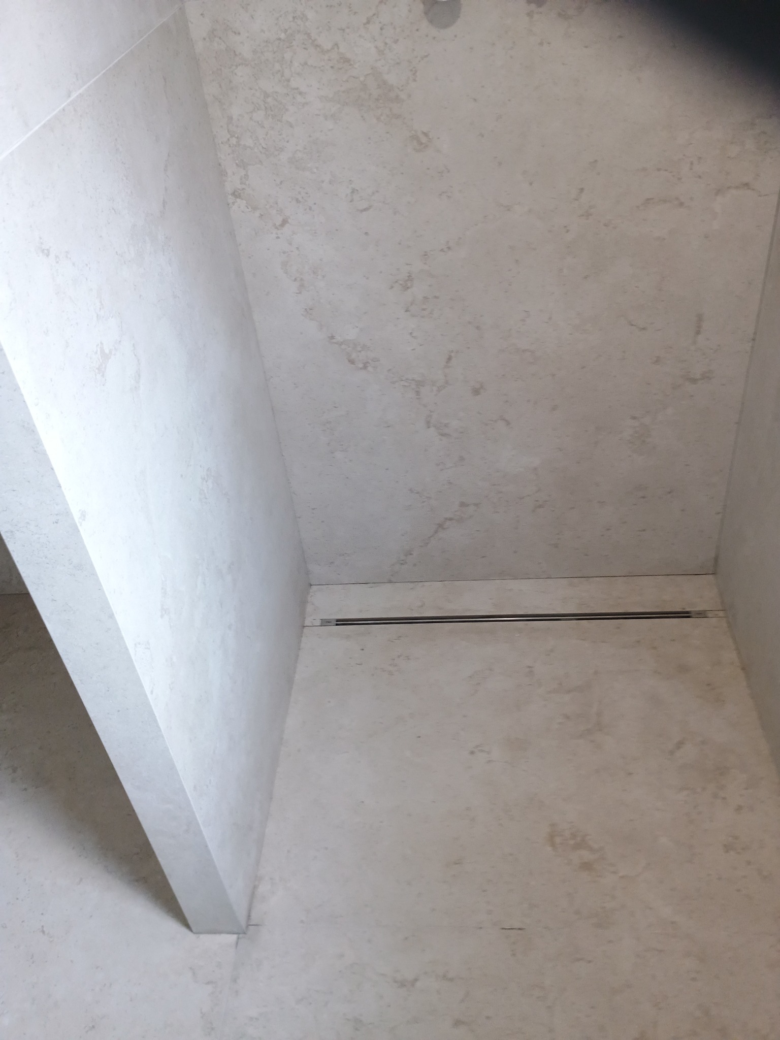 Wykończona kabina prysznicowa z odpływem liniowym i płytkami imitującymi kamień w odcieniach beżu i szarości.