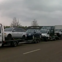 Kaskada lawet z autami osobowymi i dostawczymi w szary dzień, widok z boku na asfaltowej drodze. Auta różnych marek i kolorów.