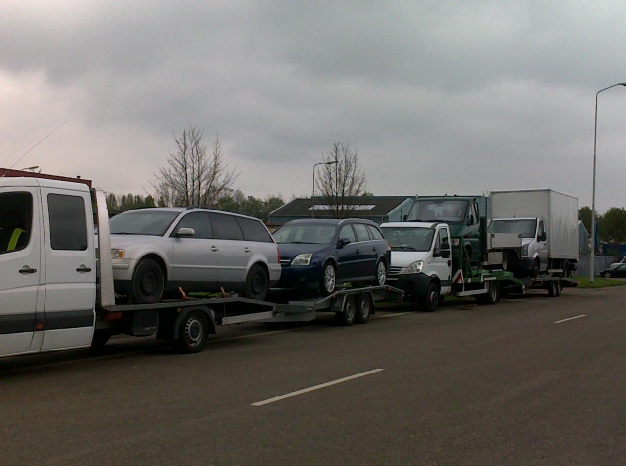 Kaskada lawet z autami osobowymi i dostawczymi w szary dzień, widok z boku na asfaltowej drodze. Auta różnych marek i kolorów.