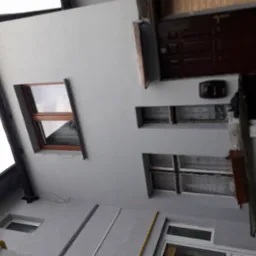 Świeżo pomalowana elewacja budynku w odcieniach szarości, widoczne okna z brązowymi ramami i brązowe drzwi wejściowe, ujęcie z dołu ukazujące detale wykończenia.