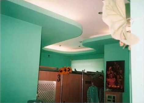 Turkusowe ściany i wielopoziomowy sufit podwieszany z oświetleniem punktowym, widoczne elementy wyposażenia wnętrza i dekoracje.