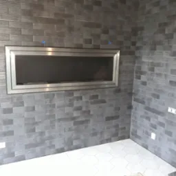 Nowoczesny, wnękowy biokominek z metalowym obramowaniem, wkomponowany w ścianę wyłożoną szarą, podłużną płytką imitującą cegłę, biała heksagonalna podłoga, realizacja w Poznaniu.