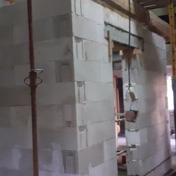 Buzdys Usługi Budowlane - Wnętrze w trakcie budowy z białych bloczków, widoczne podpory i prowizoryczne oświetlenie, surowy stan.