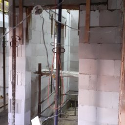 Buzdys Usługi Budowlane - Wnętrze domu w trakcie budowy z białych bloków, widoczne podpory stropowe, instalacje elektryczne i fragmenty rusztowań.