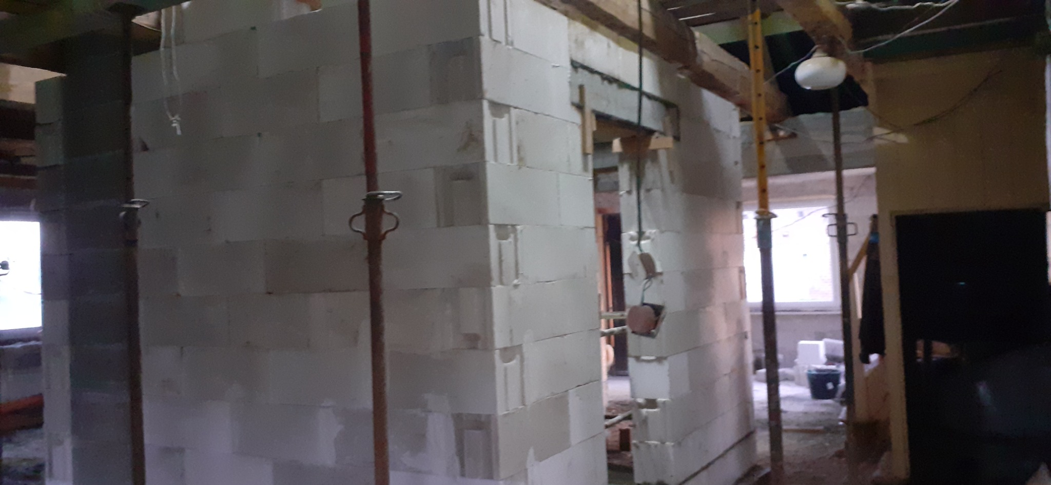 Wnętrze w trakcie budowy z białych bloczków, widoczne podpory i prowizoryczne oświetlenie, surowy stan.