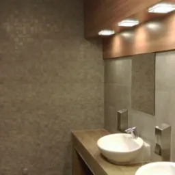 Wykończona łazienka z umywalkami nablatowymi, lustrami i mozaiką na ścianie, oświetlona punktowymi lampami. Widoczny fragment drzwi wejściowych.