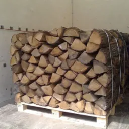 Rzędami ułożone, pocięte kawałki drewna na palecie wewnątrz przestrzeni ładunkowej, zabezpieczone białym sznurkiem.