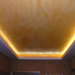 Dekoracyjny sufit z oświetleniem LED wzdłuż krawędzi, wykończony w odcieniach złota i beżu, tworzący ciepłą atmosferę w pomieszczeniu.