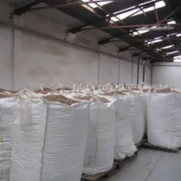 Rząd białych, worków typu big bag wypełnionych pelletem, ustawionych na paletach w hali magazynowej z metalową konstrukcją dachu i betonowymi ścianami.