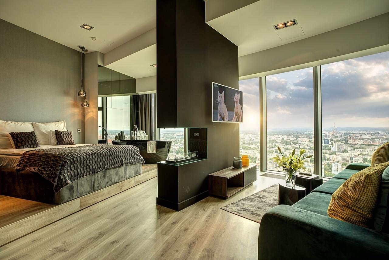 Nowoczesny apartament z panoramicznym widokiem na miasto, z łóżkiem na podwyższeniu, czarną wanną i minimalistycznym kominkiem, telewizor z wyświetlanymi kotami.