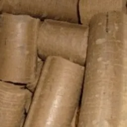 Stos cylindrycznych brykietów drzewnych z widocznymi śladami po procesie produkcji, ułożonych blisko siebie.