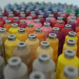 Rzędy kolorowych nici do haftowania marki Madeira, ułożone równo na białym tle, z bliska, ukazujące szeroką gamę odcieni.