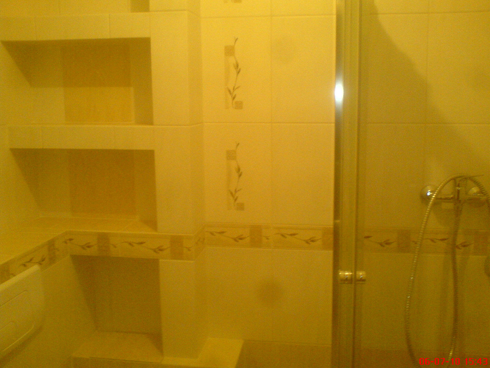 Wykończona łazienka z kabiną prysznicową, półkami w ścianie i dekoracyjnymi płytkami w odcieniach beżu.