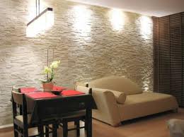 Ściana z dekoracyjną glazurą w odcieniach beżu i brązu, oświetlona punktowymi lampami, tworząca przytulne wnętrze w mieszkaniu w Warszawie. Na pierwszym planie stół z krzesłami i sofa.