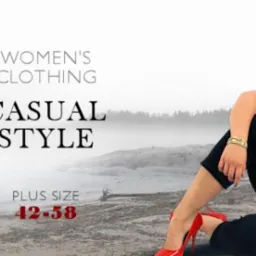 Kobieta w stroju casual w rozmiarze plus size, prezentująca bluzkę w paski, granatowe spodnie i czerwoną kamizelkę z kapturem, siedząca na tle mglistego krajobrazu z czerwonymi szpilkami.