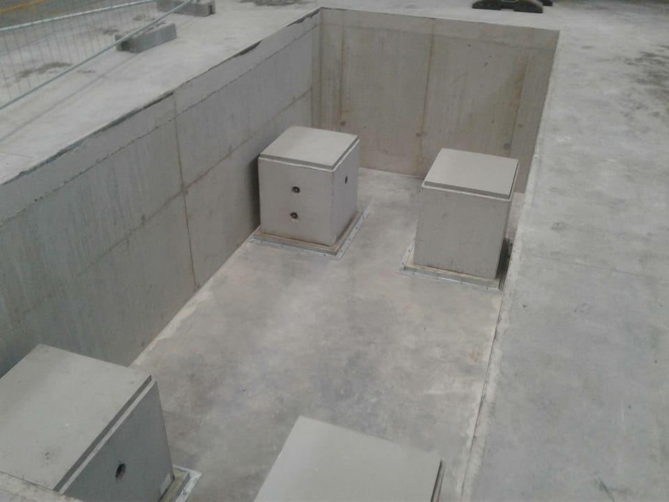 Betonowa konstrukcja podziemna z czterema włazami inspekcyjnymi na betonowej posadzce, widok z góry.