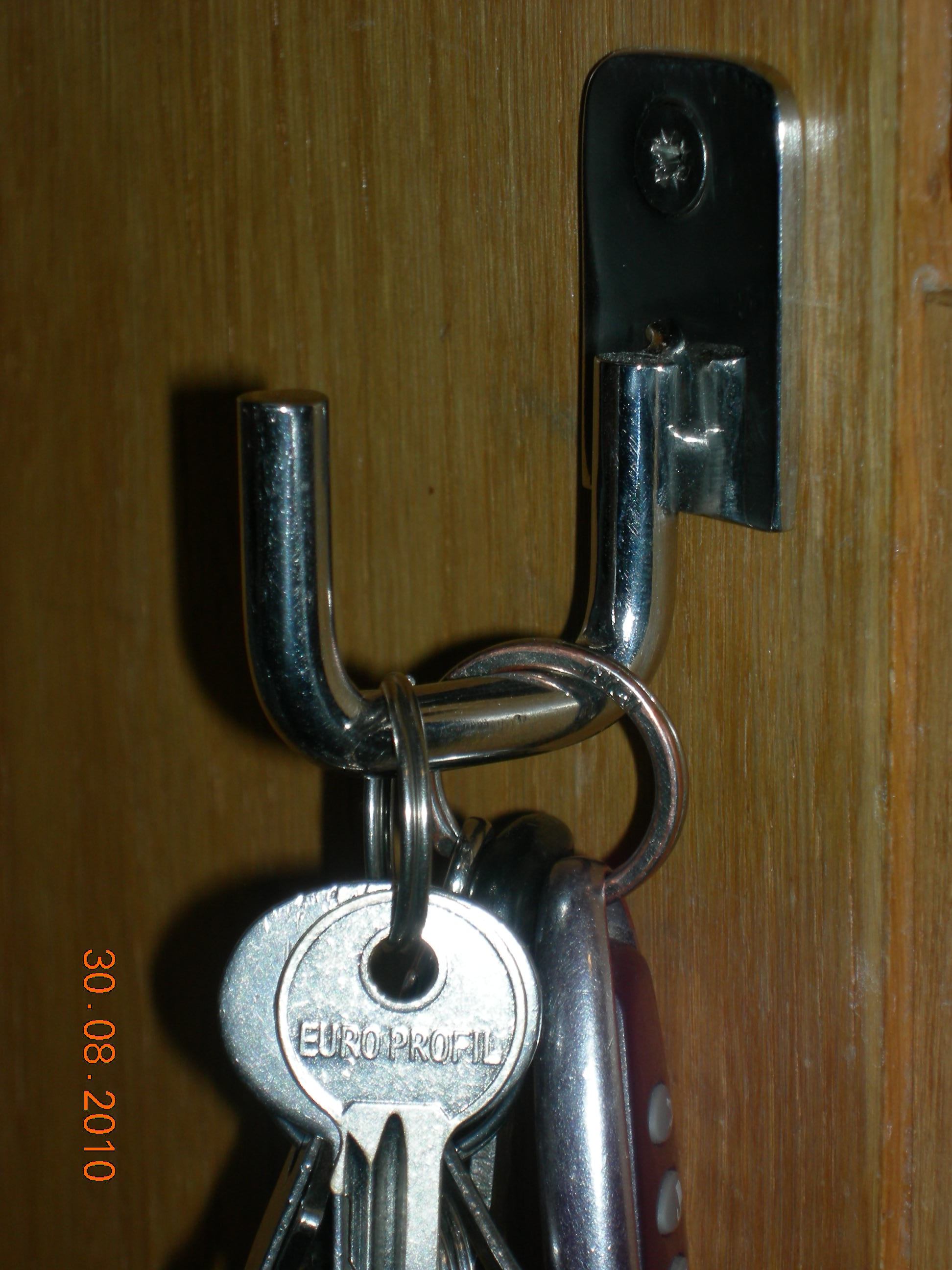 Metalowy haczyk przykręcony do drewnianej powierzchni, na którym wiszą klucze z widocznym napisem EURO PROFIL.