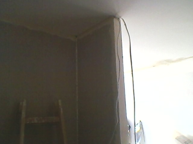 Wnętrze w trakcie prac wykończeniowych, widoczna drabina oparta o szarą ścianę, kabel zwisający ze ściany i fragment sufitu.