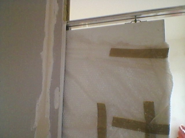 Montaż drzwi przesuwnych: widoczna prowadnica, tymczasowe zabezpieczenie skrzydła folią bąbelkową, ślady szpachlowania na ścianie.