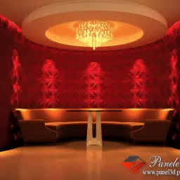 Czerwone panele 3D z okrągłym wzorem na ścianie, oświetlone od góry, z narożną sofą i stolikiem w eleganckim wnętrzu z żyrandolem.