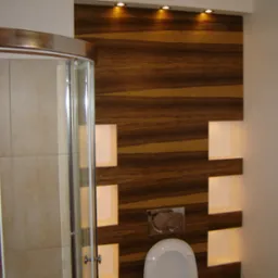 Nowoczesna łazienka z kabiną prysznicową z chromowanymi detalami i dekoracyjną ścianą z podświetlanymi niszami w odcieniach brązu.