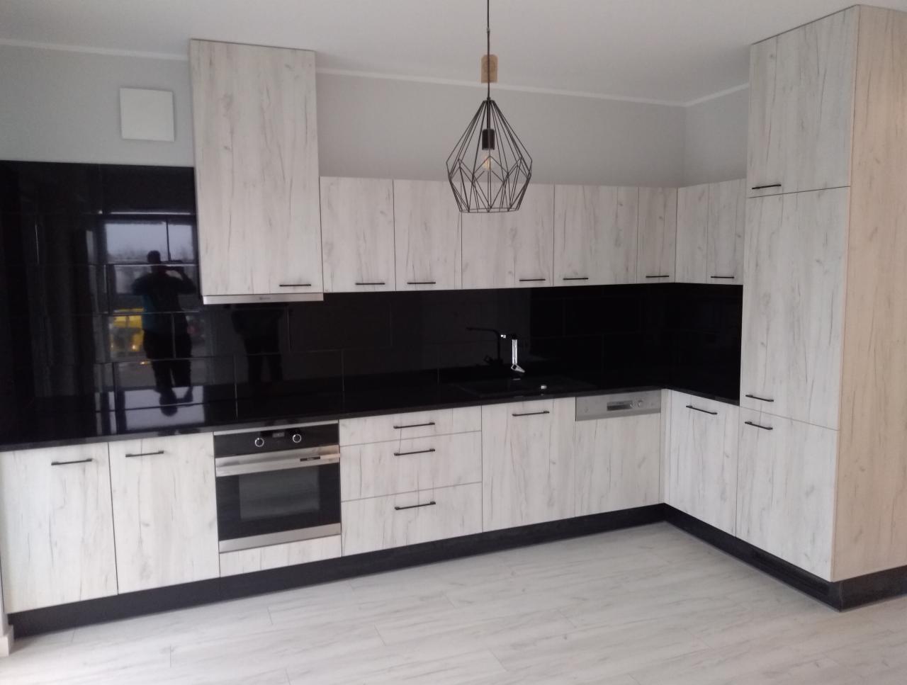 Jasna kuchnia z frontami imitującymi drewno, czarny blat i backsplash, designerska lampa wisząca