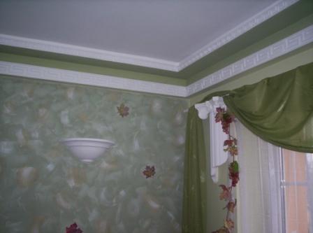 Wnętrze pokoju po malowaniu: ściana w odcieniach zieleni z motywem liści, biała lampa ścienna w kształcie misy, zielone zasłony z dekoracją z liści, biały sufit z dekoracyjnymi listwami.