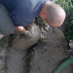 MetalMix - Mężczyzna w trakcie wiercenia studni, ręcznie wybiera błoto z otworu, obok widoczny fragment wiertnicy.
