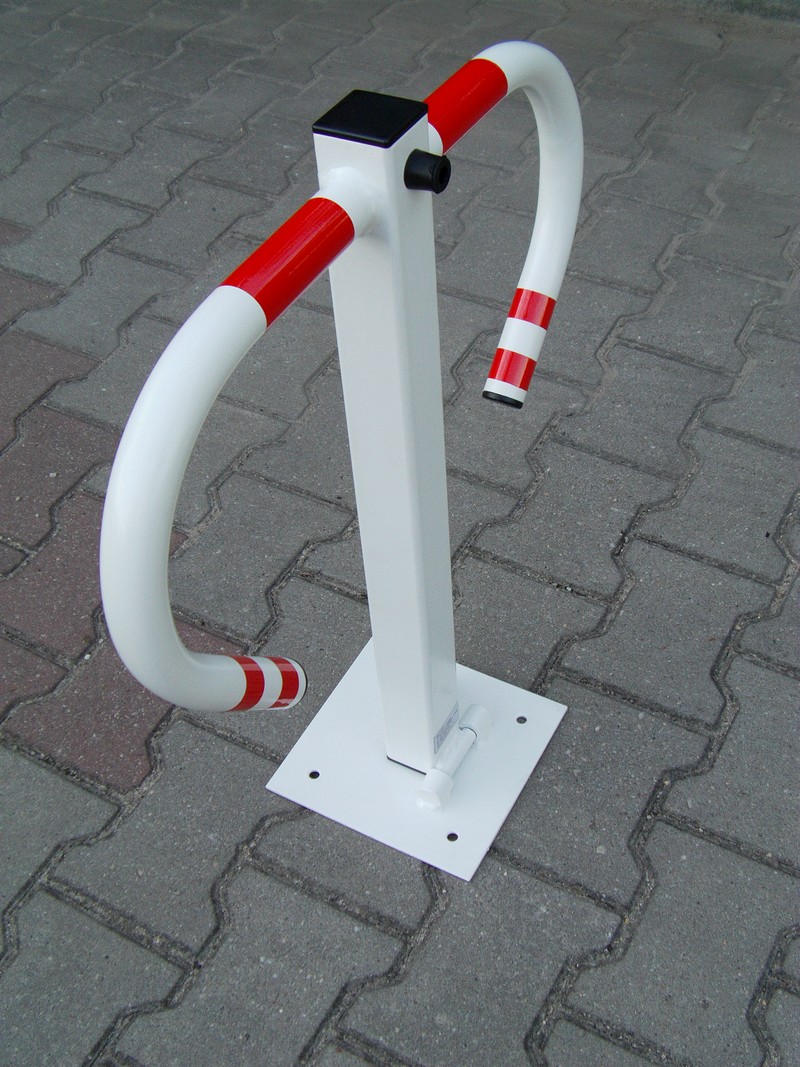 Składana, biała blokada parkingowa z elementami w kolorze czerwonym, zamontowana na kostce brukowej.