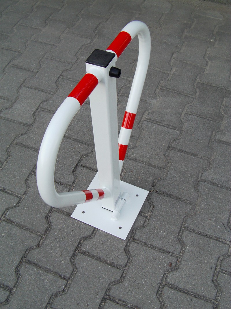 Składana blokada parkingowa w kolorze białym z czerwonymi pasami, zamontowana na szarej kostce brukowej.