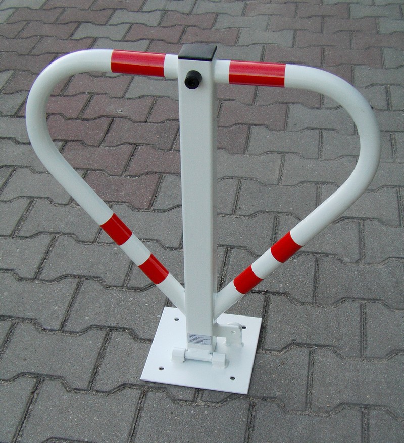 Składana, biała blokada parkingowa Triangle z czerwonymi odblaskowymi pasami, zamontowana na szarej kostce brukowej.