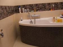 Biała wanna obudowana czarną mozaiką w łazience z beżowymi ścianami i dekoracyjnym pasem płytek nad wanną.