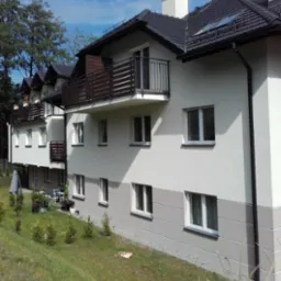 Nowoczesny, wielorodzinny budynek z balkonami w Bielsku-Białej, z jasną elewacją i ciemną stolarką okienną, otoczony zielenią.