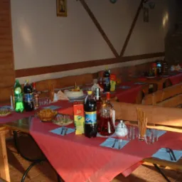 Ustawione stoły z napojami, przekąskami i ciastem w drewnianej sali z ławami, przygotowane na imprezę.