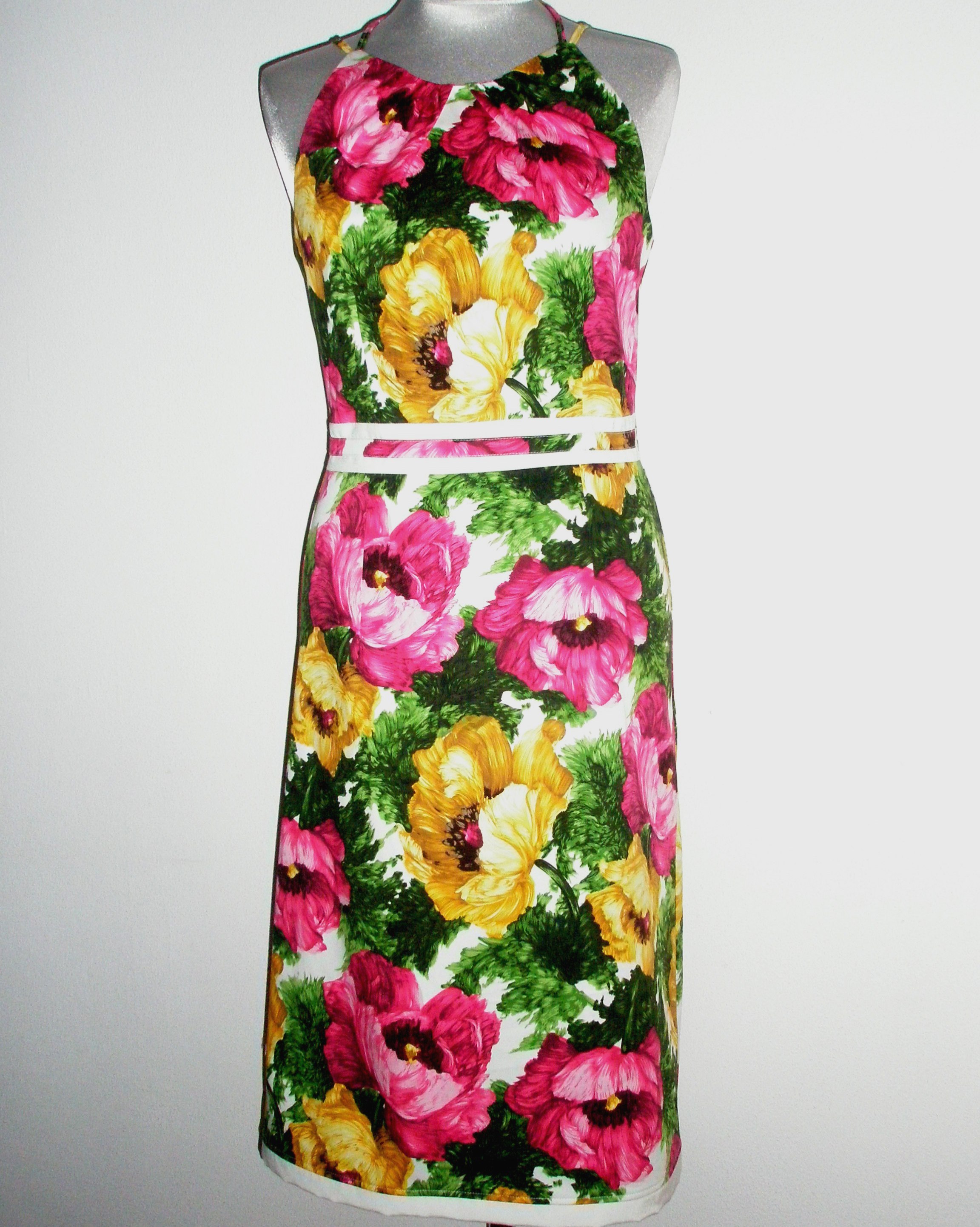 Sukienka letnia na manekinie, wzór w duże, różowe i żółte kwiaty z zielonymi liśćmi na białym tle, z białym paskiem w talii.