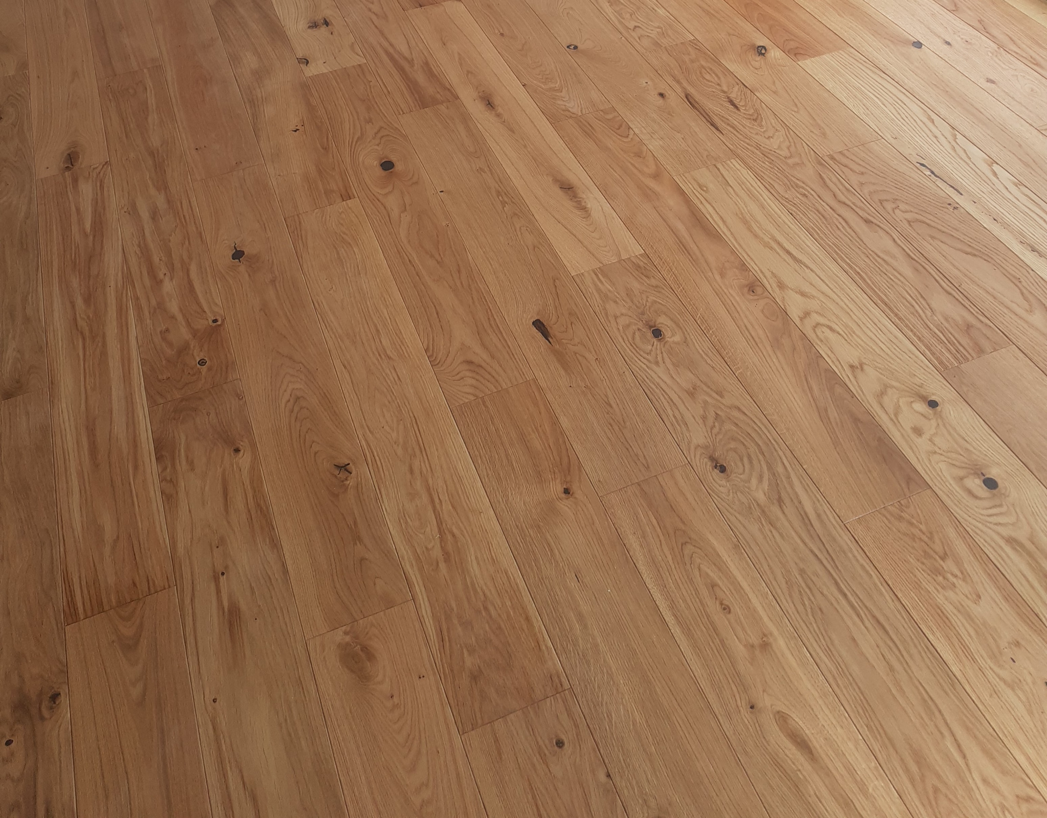 Ukośny widok na ułożoną, lakierowaną podłogę z jasnego drewna z widocznymi naturalnymi sękami i słojami.