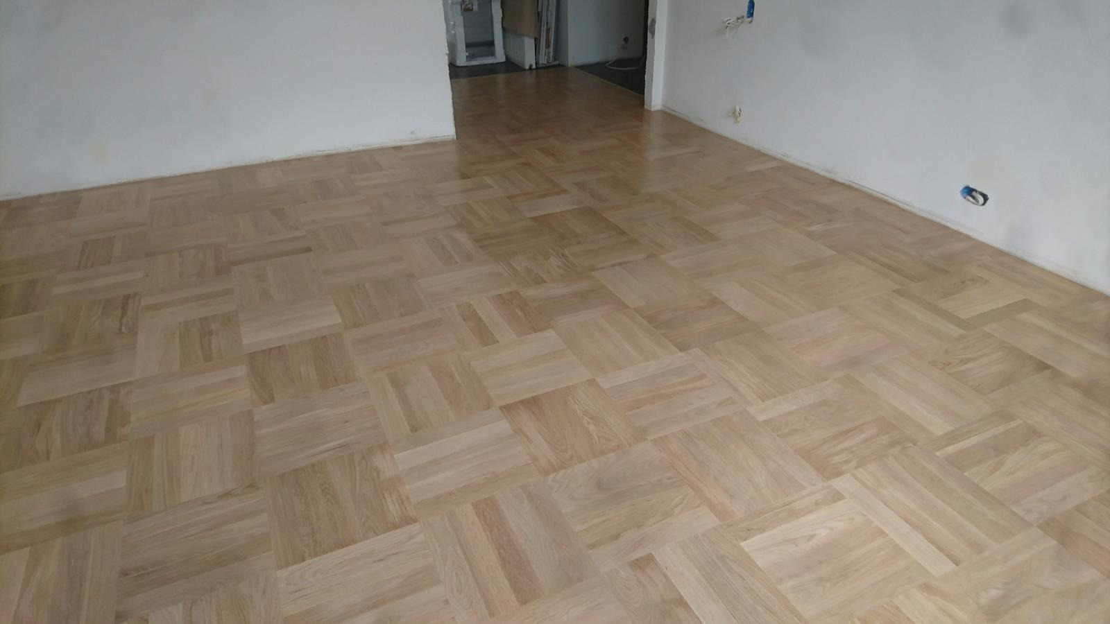 Ułożona parkietowa podłoga w jodełkę w odnowionym pokoju w Bliżynie, widoczne niedokończone ściany i gniazdka elektryczne.