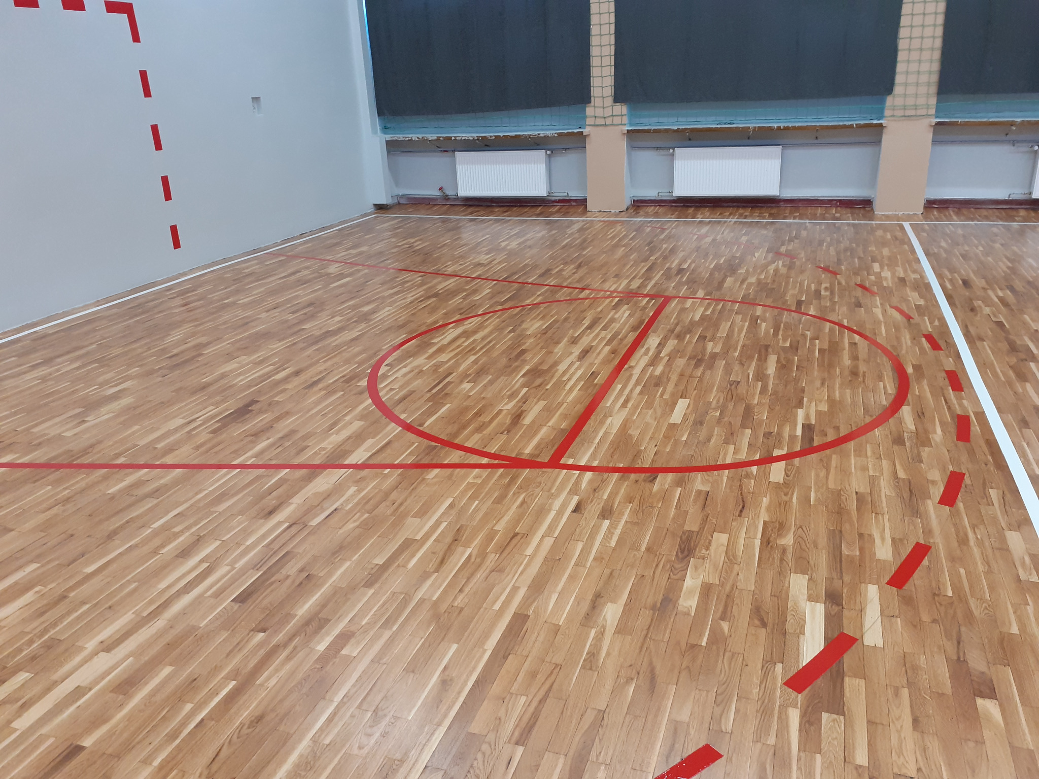 Drewniana podłoga hali sportowej z czerwonymi liniami boiska do gry, widok z góry na parkiet z wyraźnym wzorem ułożenia klepek.