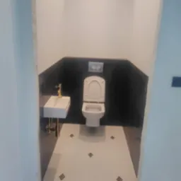 Nowoczesna toaleta w trakcie wykańczania: biała umywalka z złotą armaturą, wisząca muszla klozetowa, czarne mozaikowe płytki na ścianie i biała podłoga z dekoracyjnymi wstawkami.