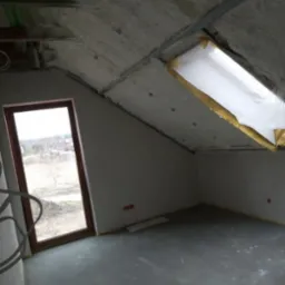 Poddasze w trakcie ocieplania pianą, widoczne okno dachowe z folią ochronną, metalowe profile pod płytę karton gips i szara wylewka na podłodze.