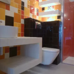 Nowoczesna łazienka z umywalką na tle mozaiki z płytek w odcieniach pomarańczy i czerni, oraz toaletą w kolorze białym. Widoczna kabina prysznicowa.