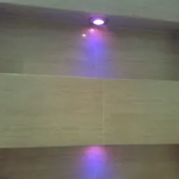 Beżowe płytki ceramiczne z wnękami oświetlonymi fioletowym światłem punktowym w łazience.