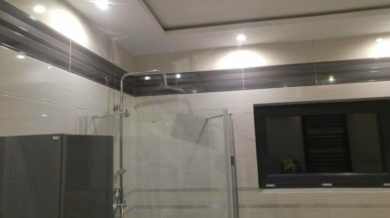 Nowoczesna łazienka po remoncie z kabiną prysznicową typu walk-in, wykończona jasnymi płytkami z poziomym, ciemniejszym pasem dekoracyjnym i oknem w czarnej ramie.