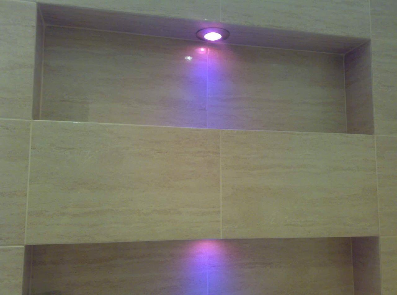 Beżowe płytki ceramiczne z wnękami oświetlonymi fioletowym światłem punktowym w łazience.