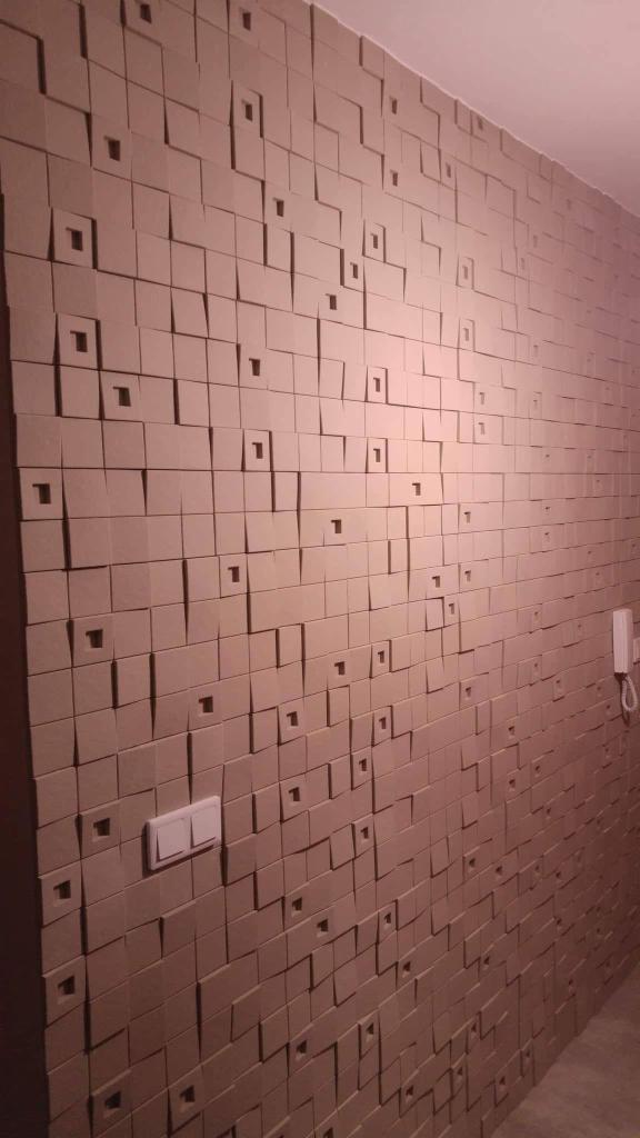 Ściana wykończona panelami 3D w odcieniach beżu z kwadratowymi wgłębieniami, widoczny włącznik światła i telefon na ścianie.