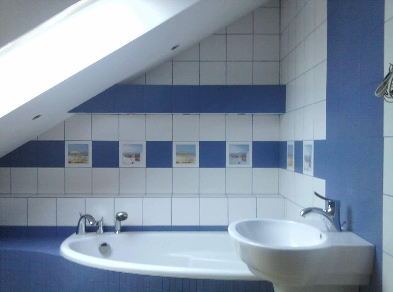 Łazienka na poddaszu z biało-niebieskimi płytkami, dekoracyjnym pasem z obrazkami plażowymi, białą wanną i umywalką z chromowaną armaturą.