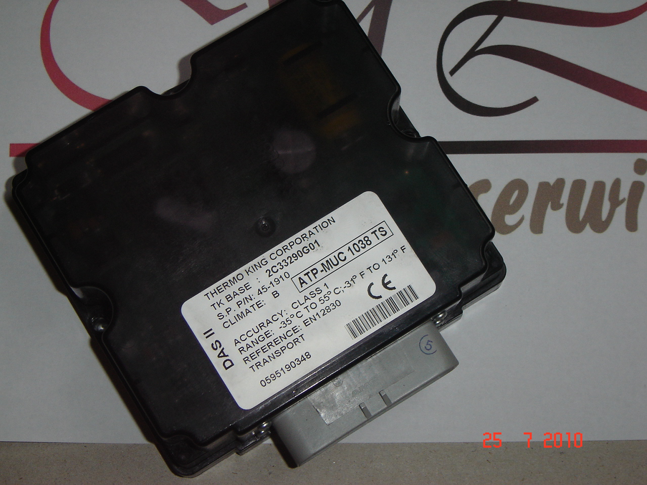 Czarna obudowa modułu sterującego Thermo King ATP-MUC 1038 TS z widoczną etykietą specyfikacji technicznej, leżąca na tle z elementami graficznymi i datą 25.7.2010.