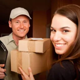 Uśmiechnięty kurier w czapce i koszuli trzymający czarny notatnik z długopisem przekazuje dwa kartonowe pudełka uśmiechniętej kobiecie w drzwiach.