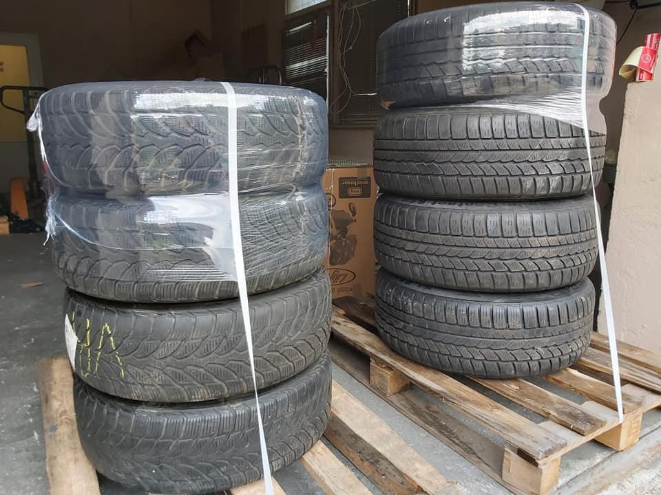 Dwa stosy opon zimowych zapakowanych w folię stretch, umieszczone na drewnianych paletach w magazynie.